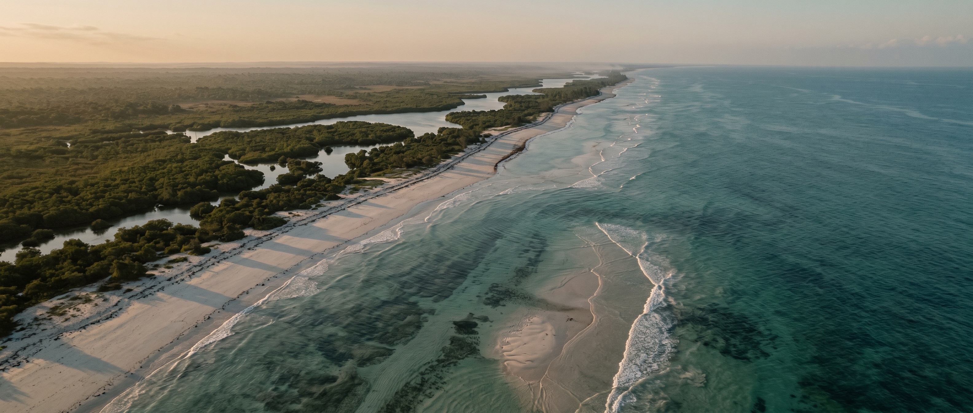 Aerial view of a low-lying Kenyan coastline at dawn — a thin strip of pale sand and mangrove-fringed shore separating turquoise shallows from the open ocean